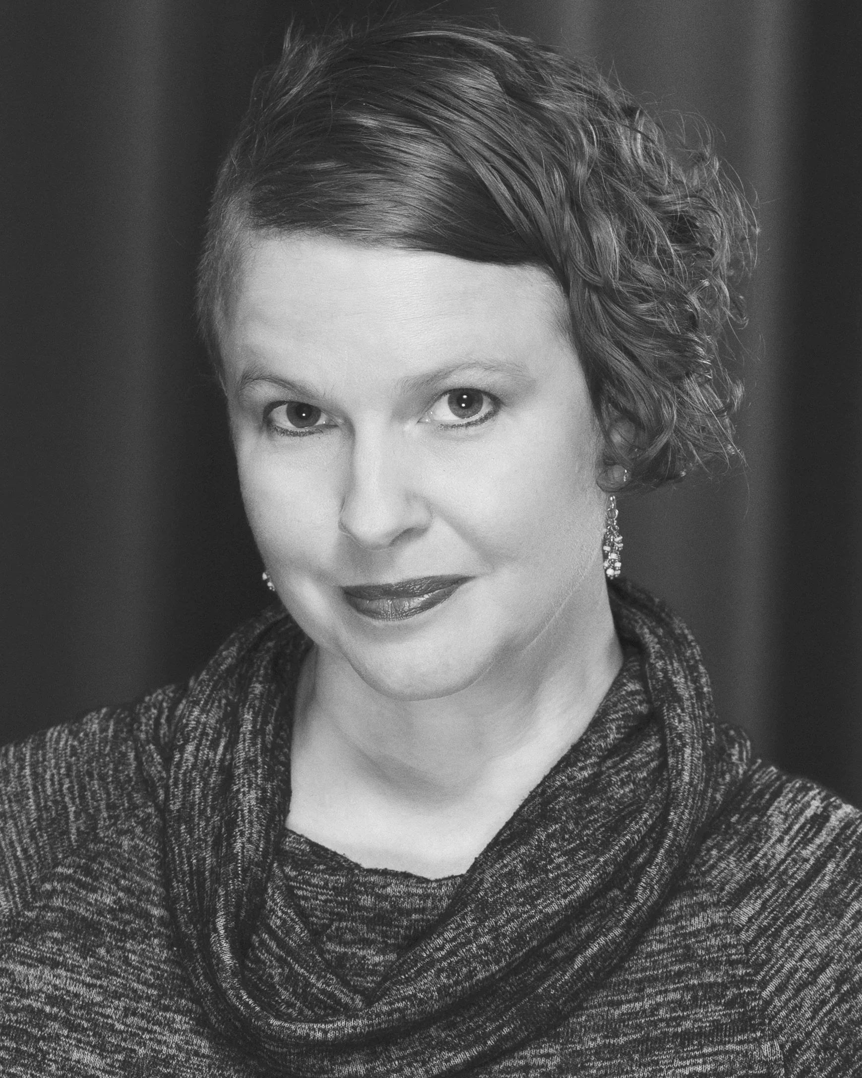 A black and white portrait of a woman with short hair, wearing earrings and a patterned top.  Mandi Wickline, actor.