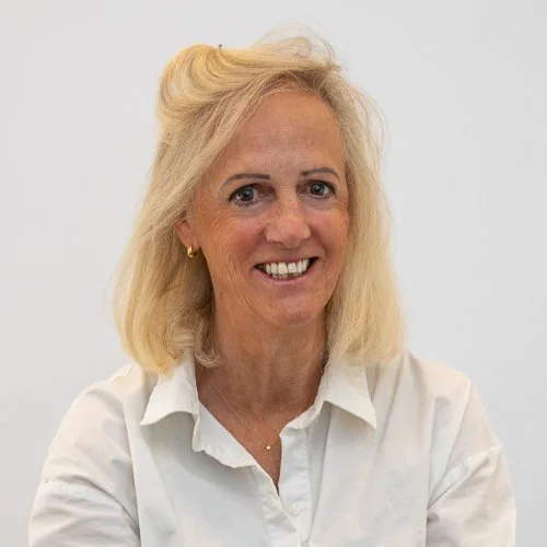 Vrouw met blonde haar, wit overhemd, glimlach, en een lichte achtergrond.