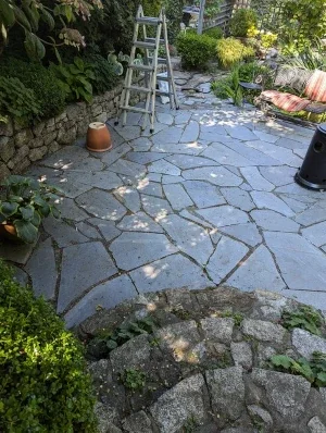 A slate flagstone patio, top-down view amidst a garden with rock walls and steps