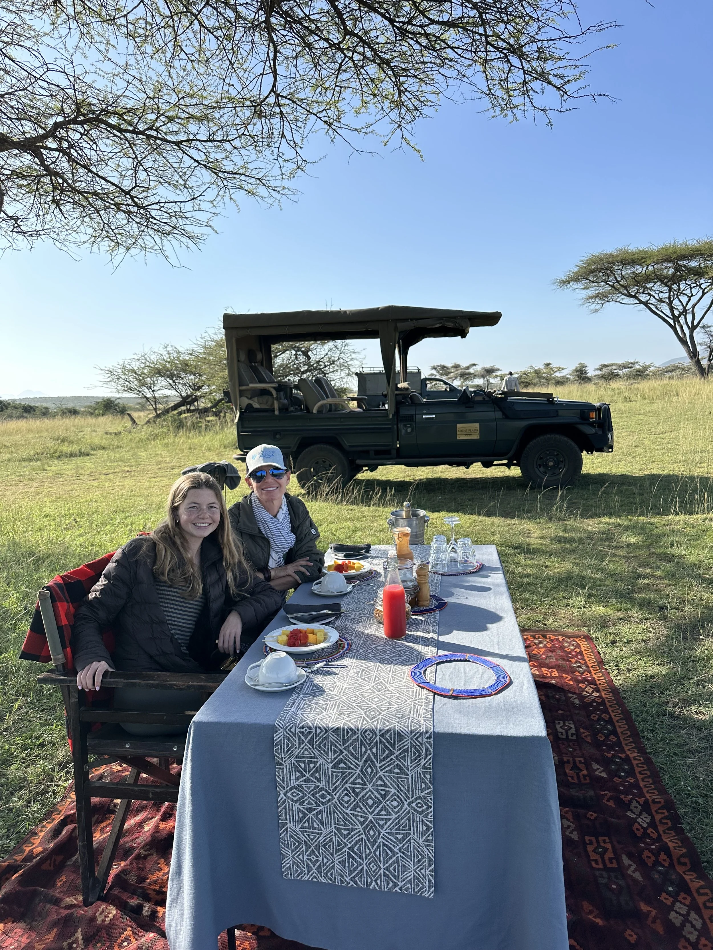 Outdoor luxury safari breakfast setup with game drive vehicle in Africa