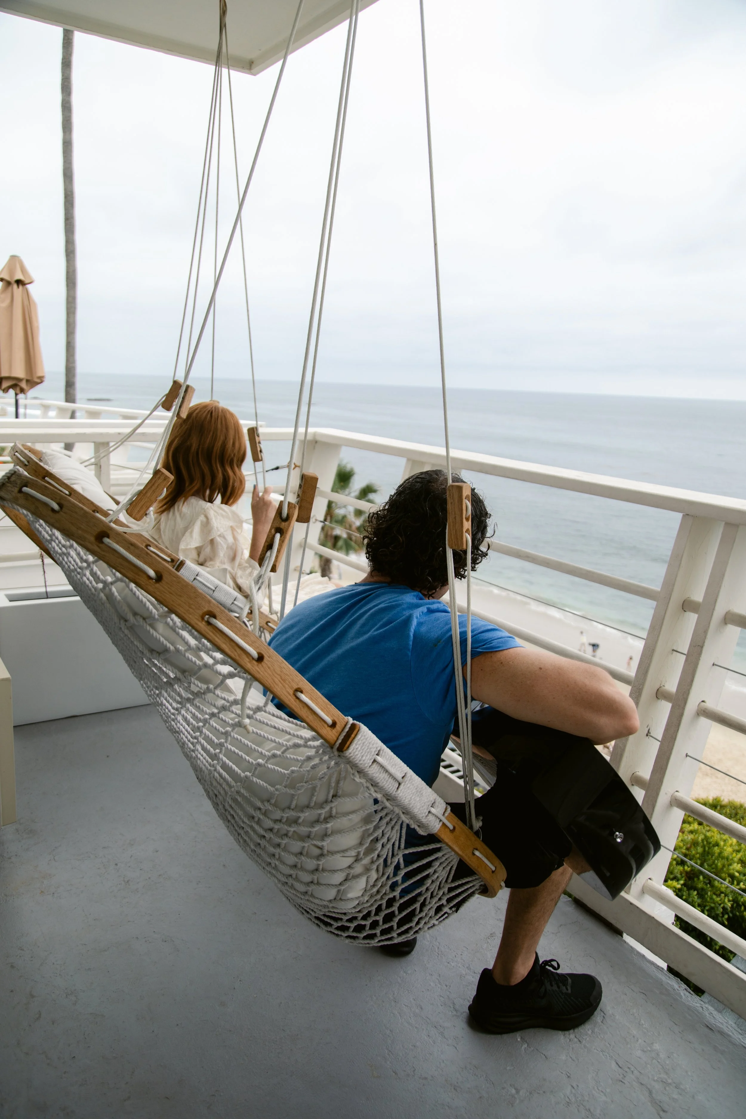 Guests relaxing on hanging swings on an oceanfront balcony at Laguna Surf Lodge in Laguna Beach.