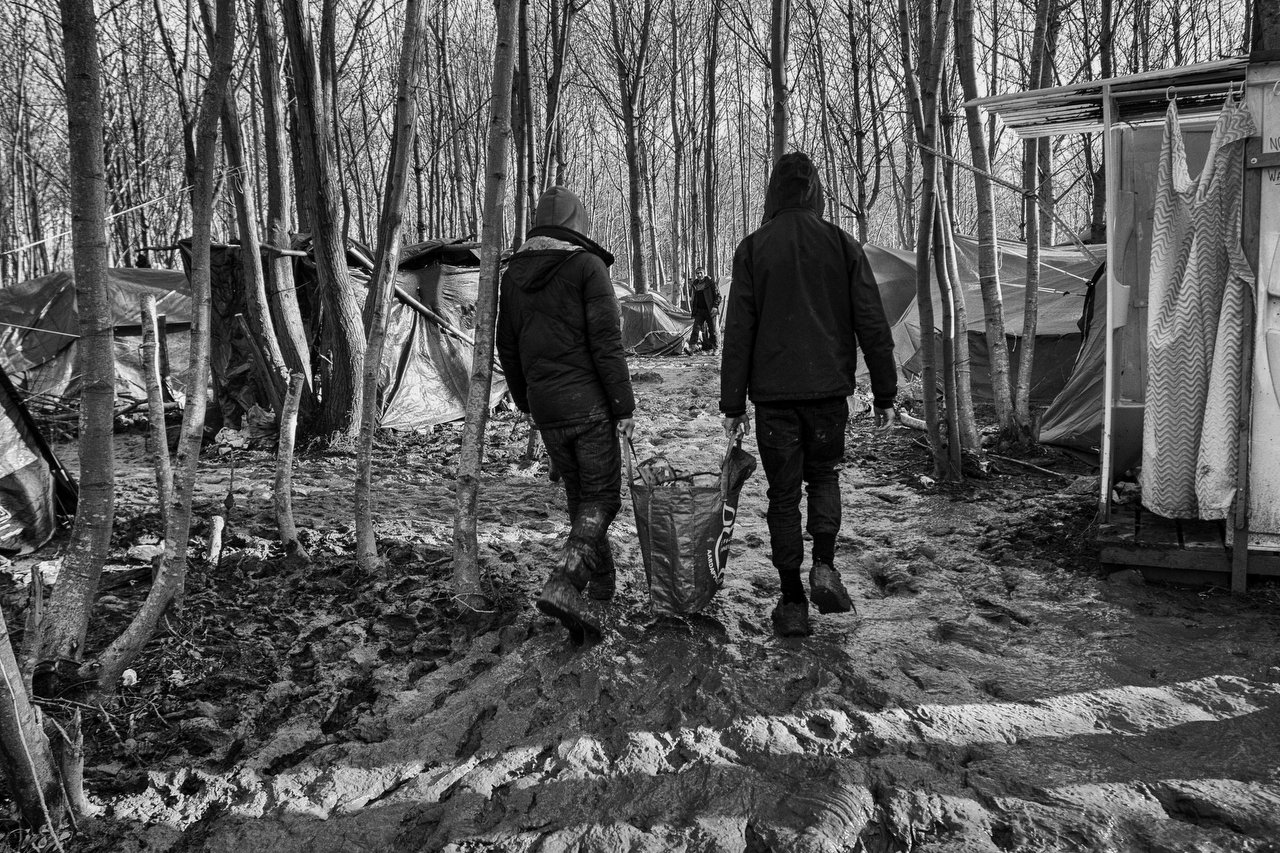  Two refugees walk in the mud with a bag of firewood for cooking at the refugee camp of Grande-Synthe, Dunkirki, France, January 8, 2016. Photo Delmi Alvarez. 