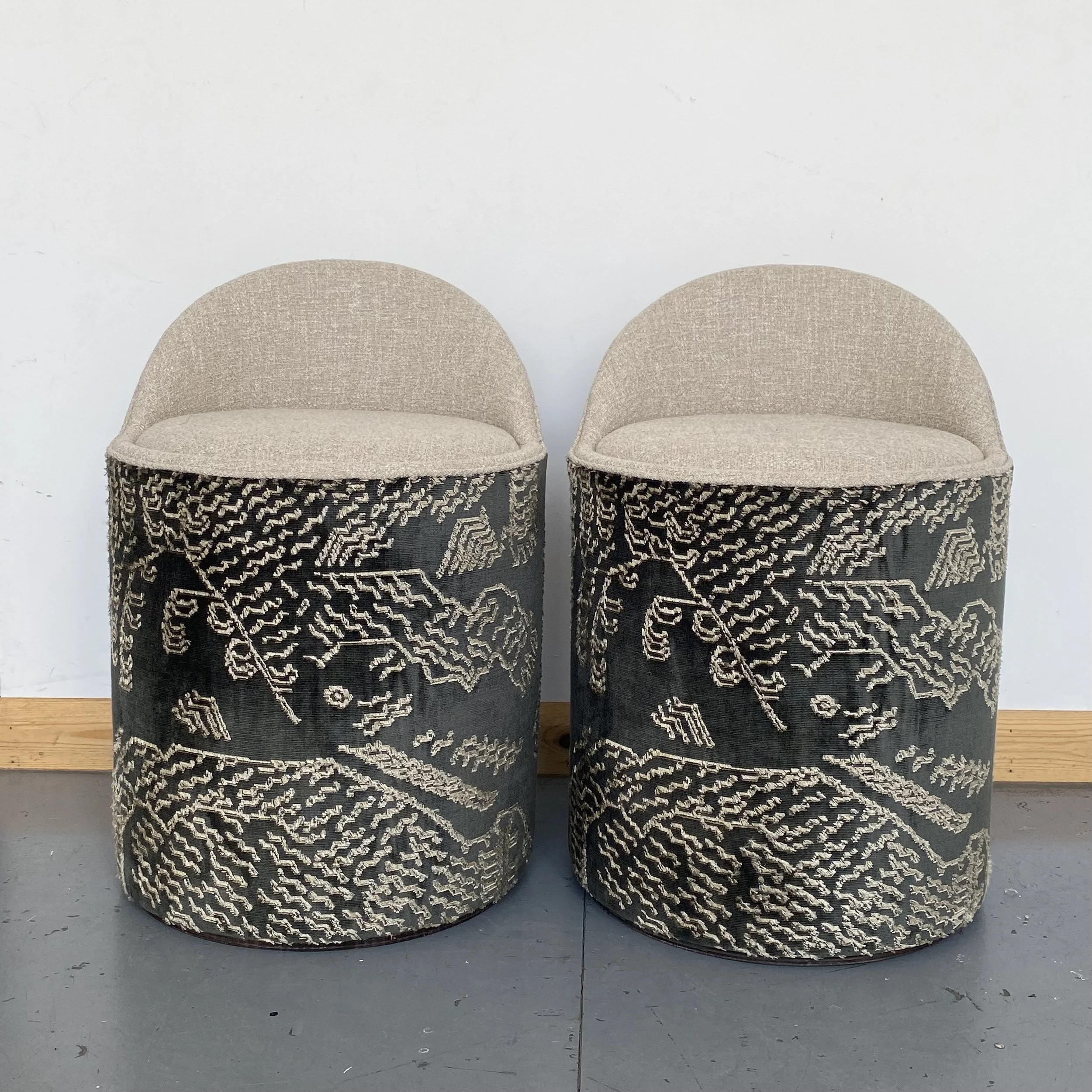 Two beige upholstered chairs with black and white patterned bases placed against a plain white wall.