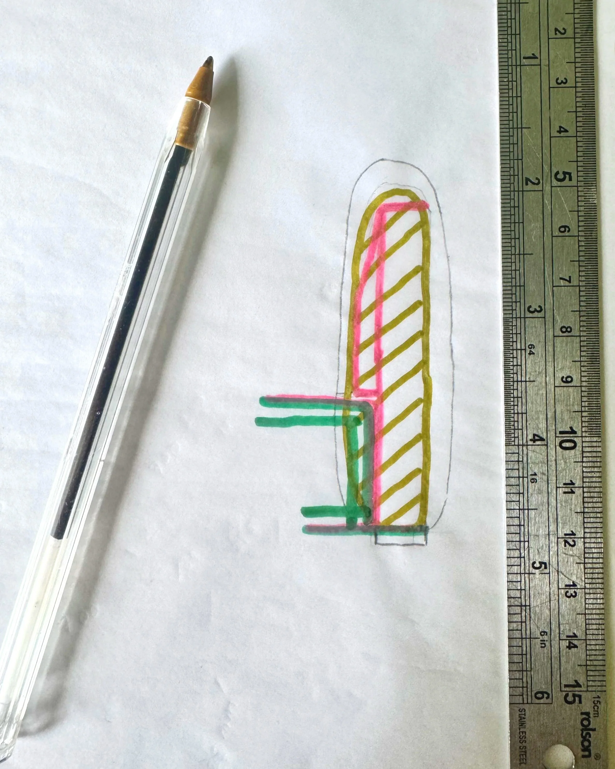 A hand-drawn sketch of sofa arm frame on a white sheet of paper, with different coloured outlines and diagonal stripes, accompanied by a ruler for scale and a pen nearby.