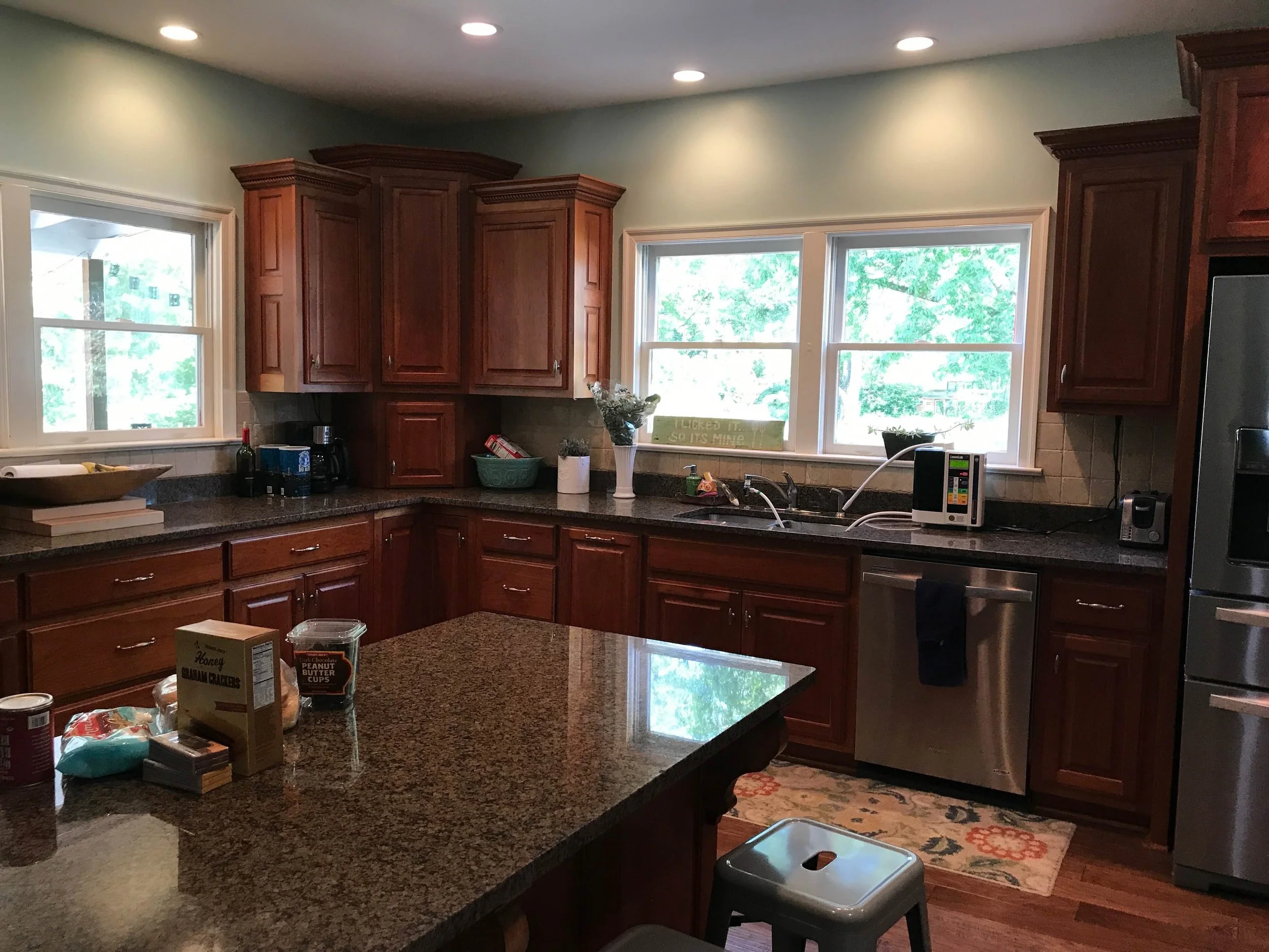 shows the old kitchen with dark wood cabinets, black countertops and shorter windows