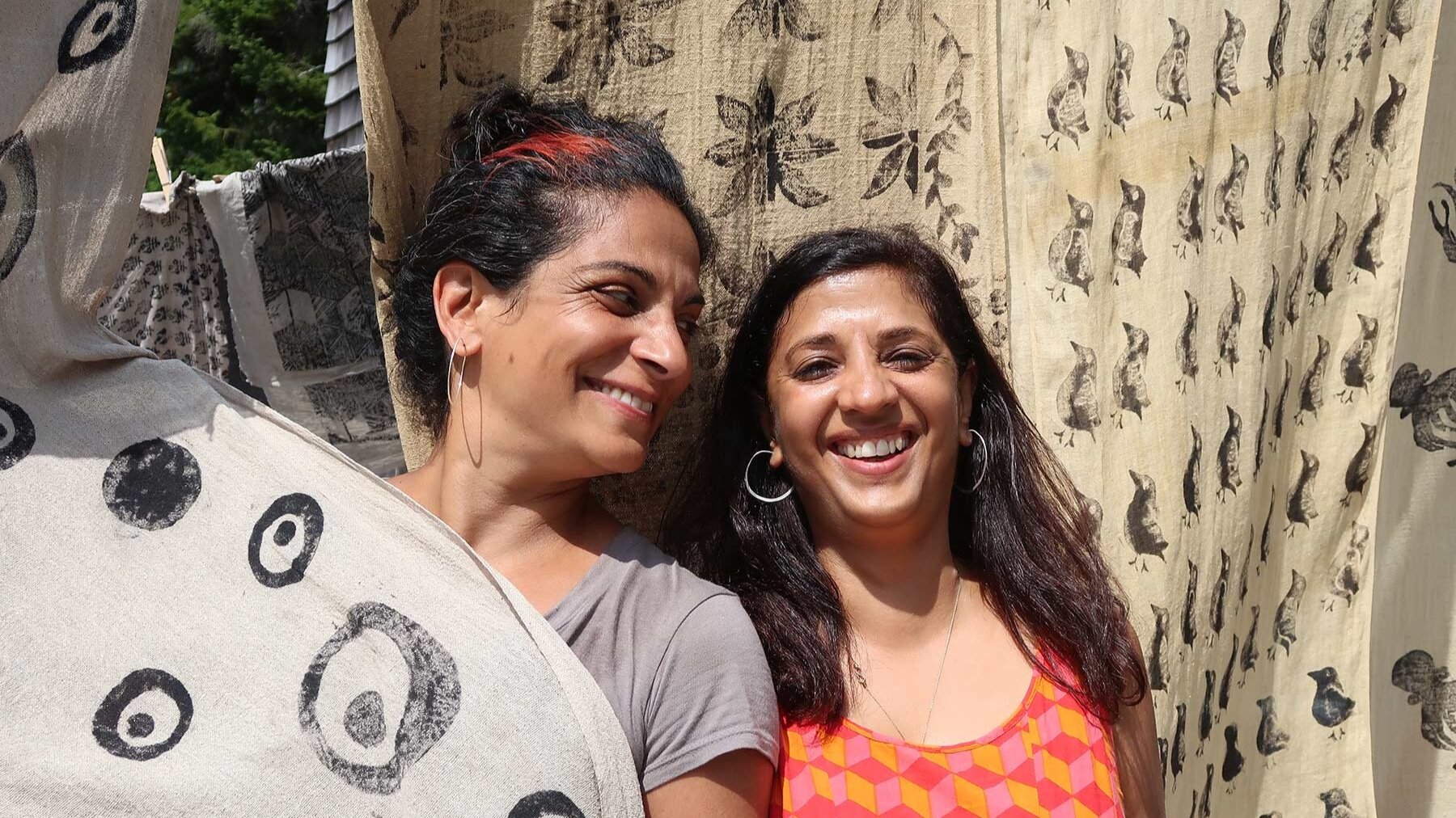 Two women smile in front of blockprinted textiles