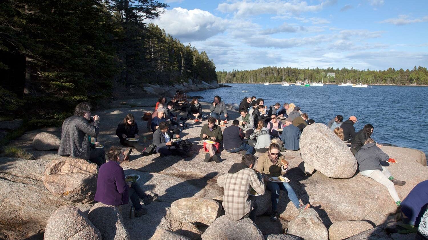 People sit on rocks near the ocean, eating lunch