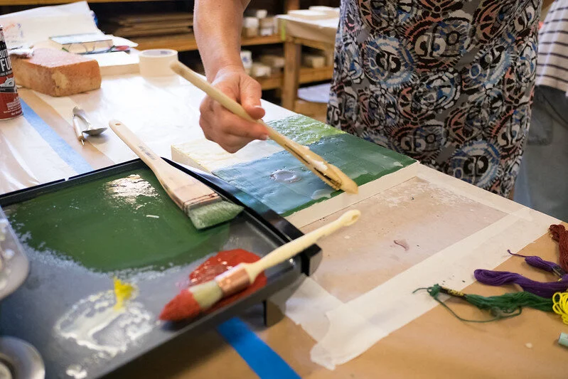 Image of person hands painting with red and green encaustic paint.