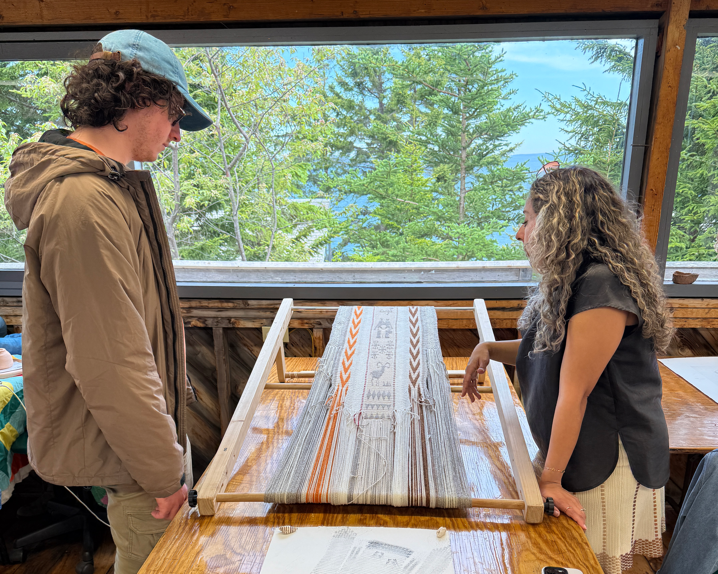 2026 Open Studio Residency_Image of two people looking at a weaving on a wood table.png