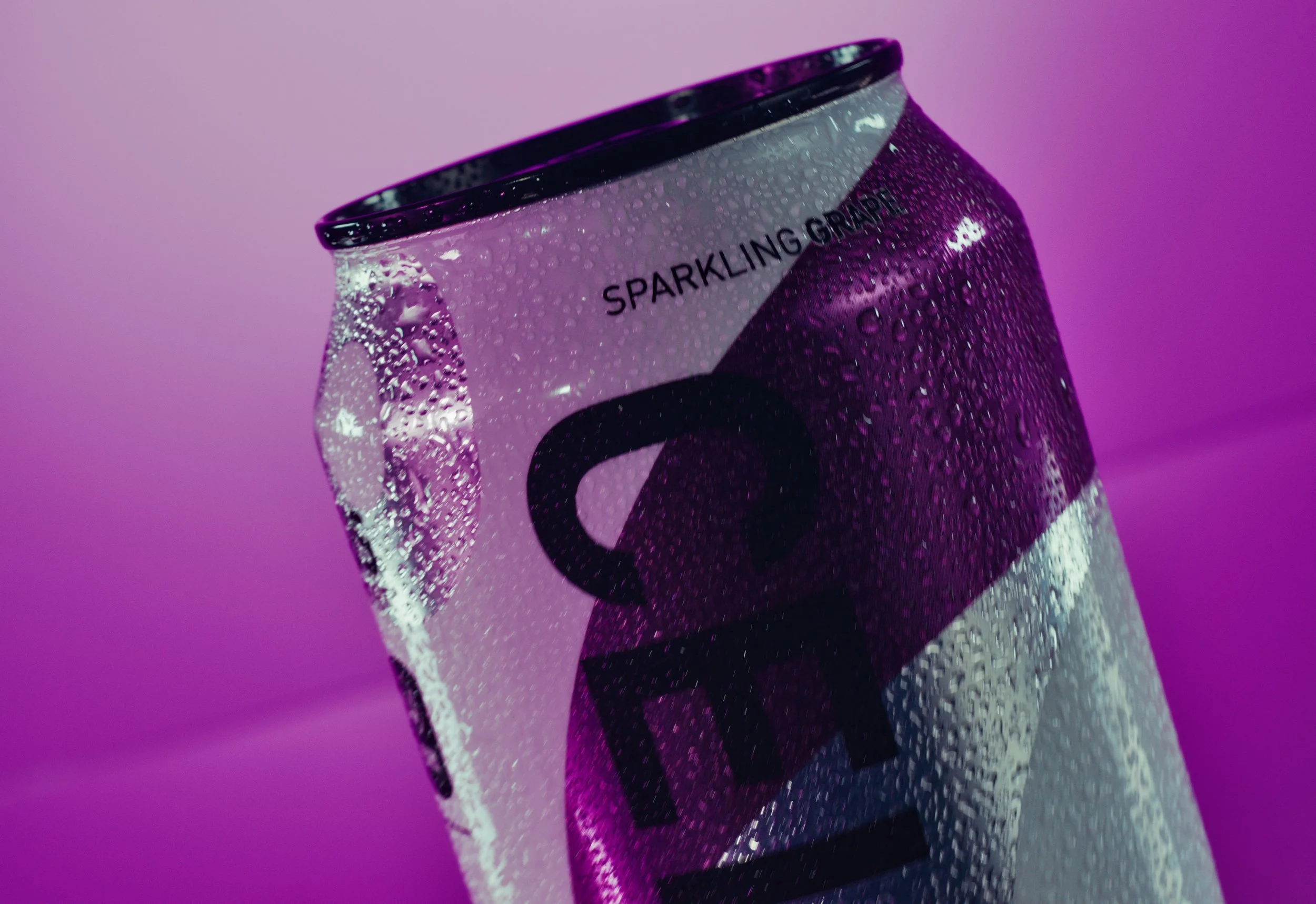 Close-up of a can of sparkling grapefruit soda with condensation, against a purple background.
