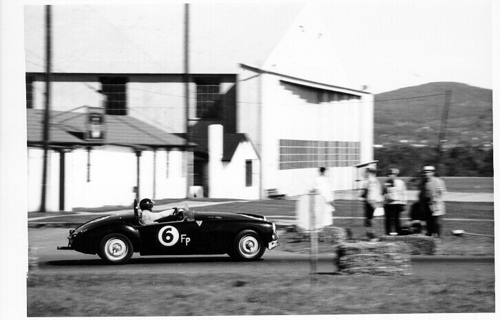 DN wearing a sweater passes a stop sign and spectators. Are they waiting to cross the street? The corner of the airport streets to a runway.