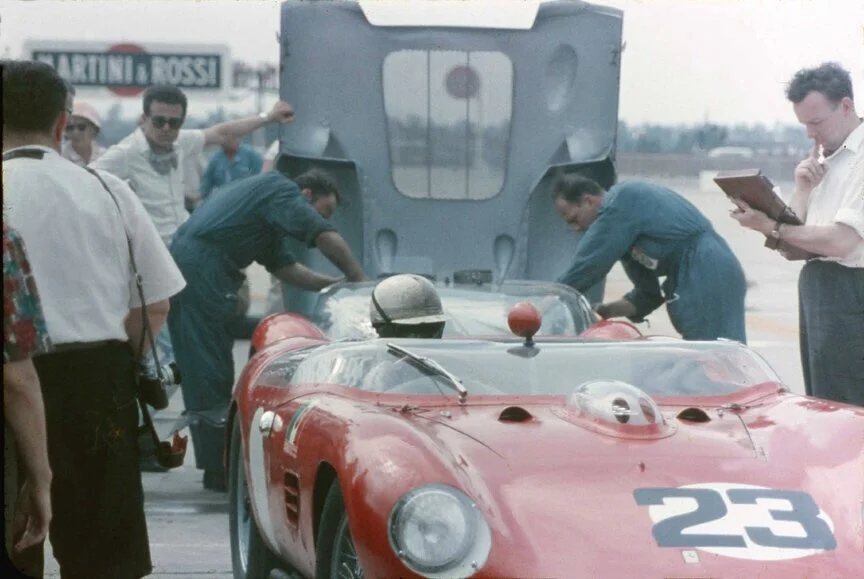 Bonnier sits in the car while mechanics check something in the engine compartment..