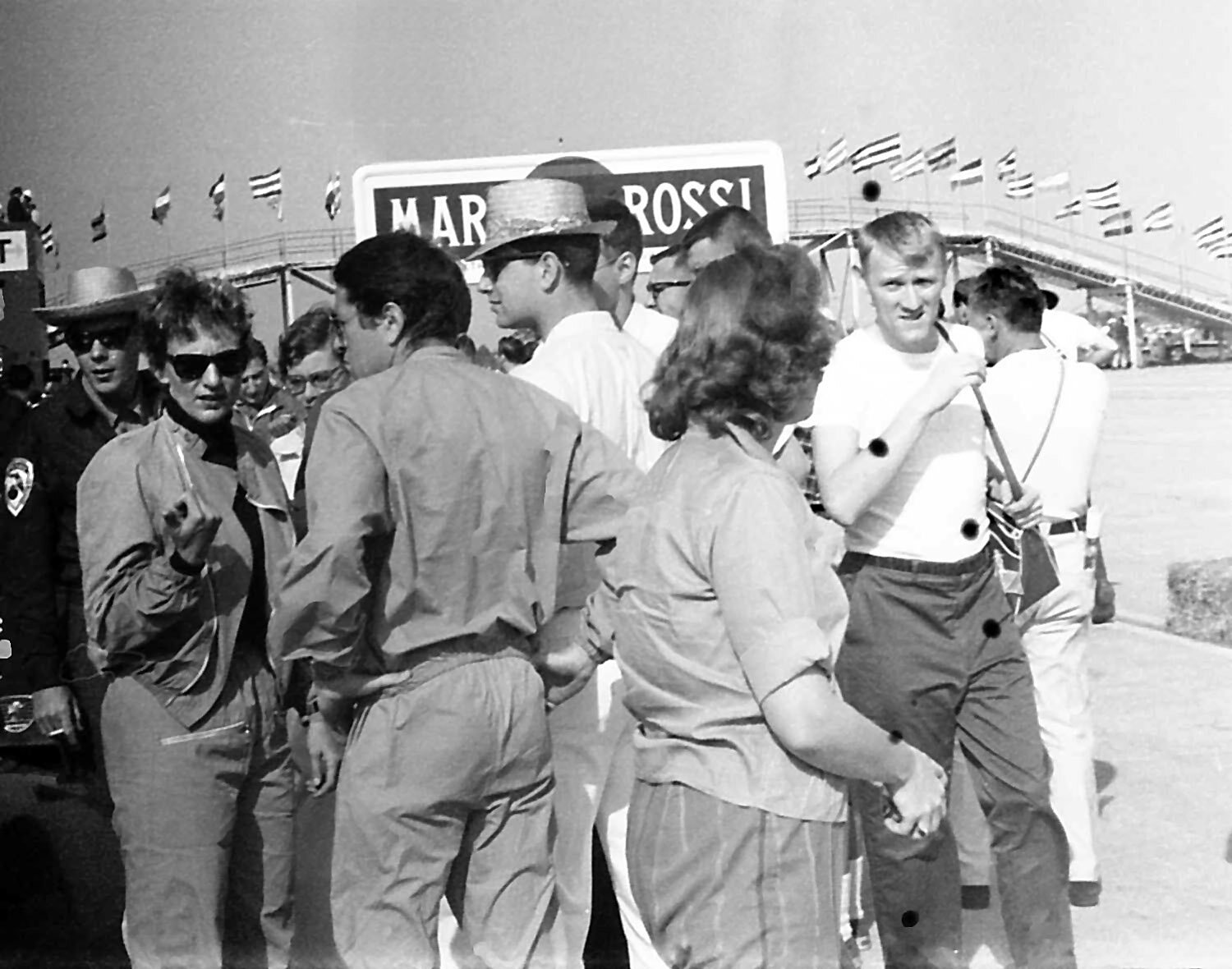 Denise McCluggage gives us a glance as Alan Eager (with his back to us) is thinking he’d rather be in a New York club jamming on the sax.