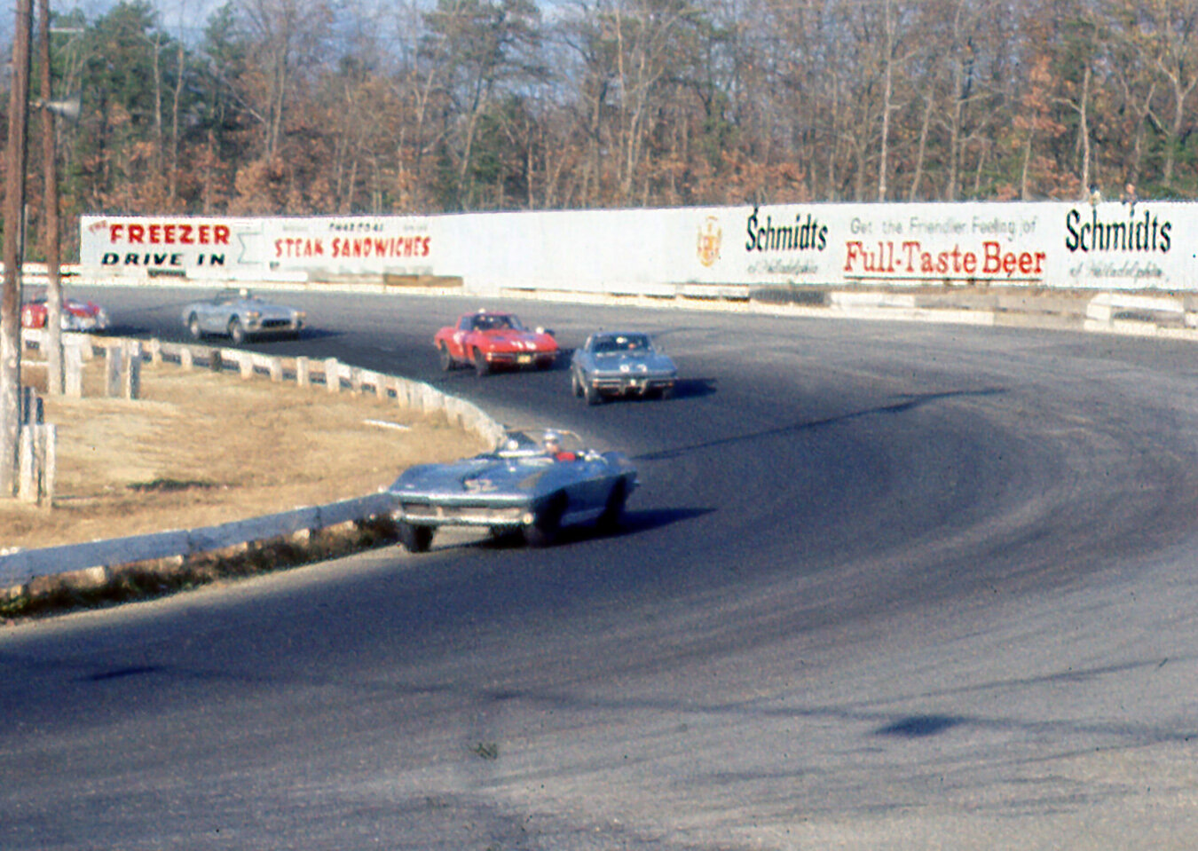 Al Loquasto’s Vette leads a pack in the afternoon race. He would finish 3rd overall. If you look to the left behind the telephone poles is Bruce Jenning;s Porsche Carrera who would pass all the Corvettes to finish 2nd.