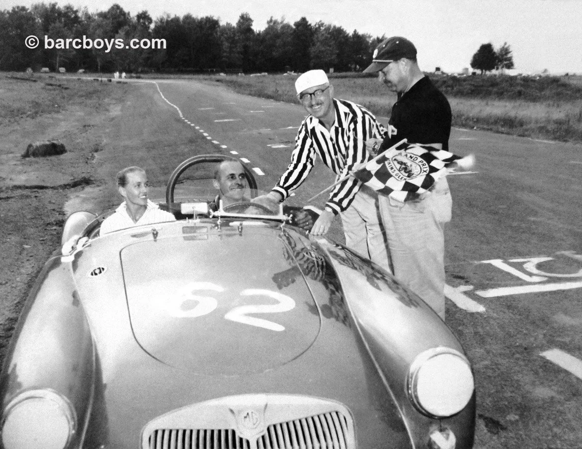 A smiling Sherm Decker and lovely wife Joan get the checkered flag and congratulations from the starter.