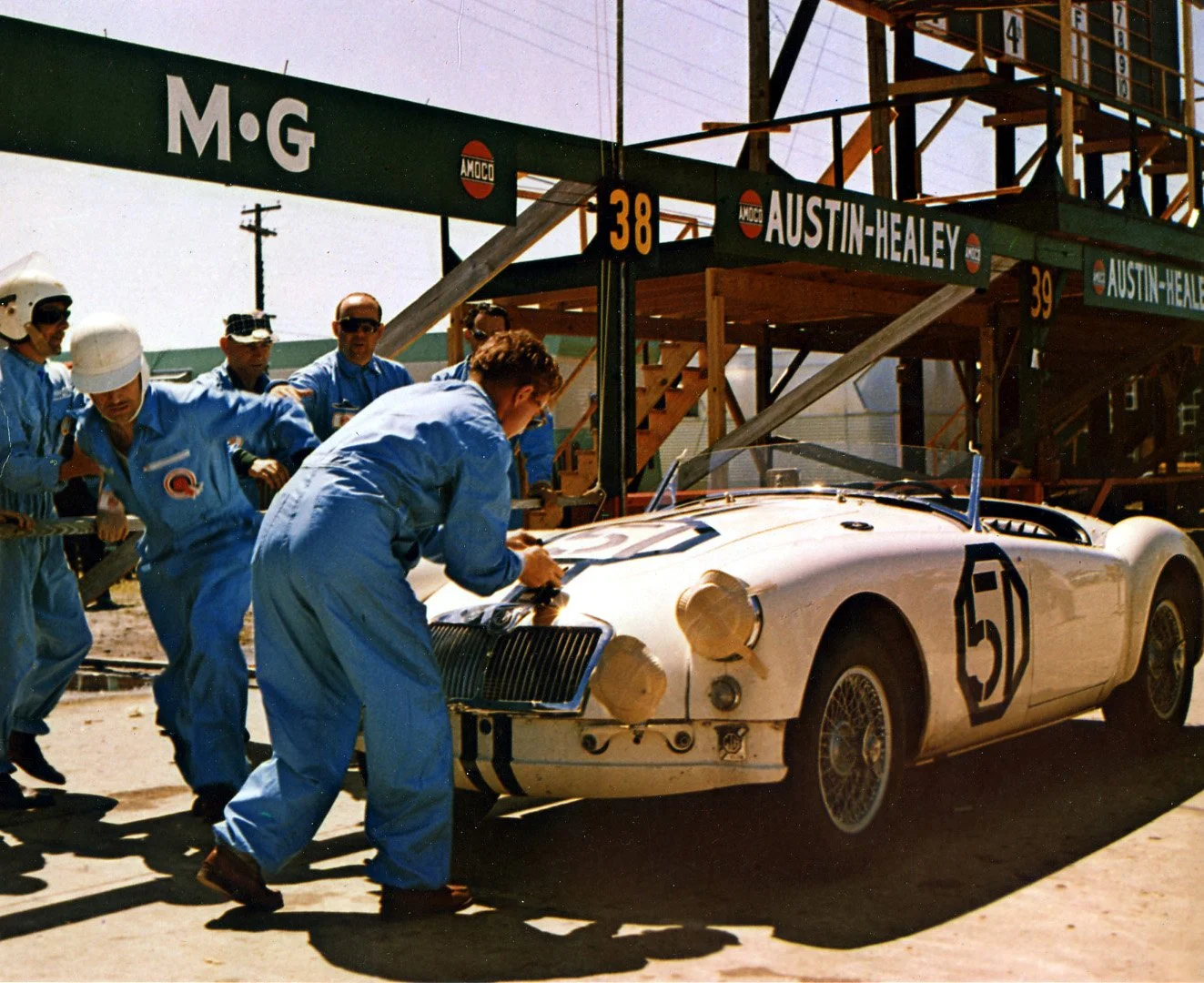  Gus Ehrman is running around the car to take off as a mechanic secures the hood strap. 