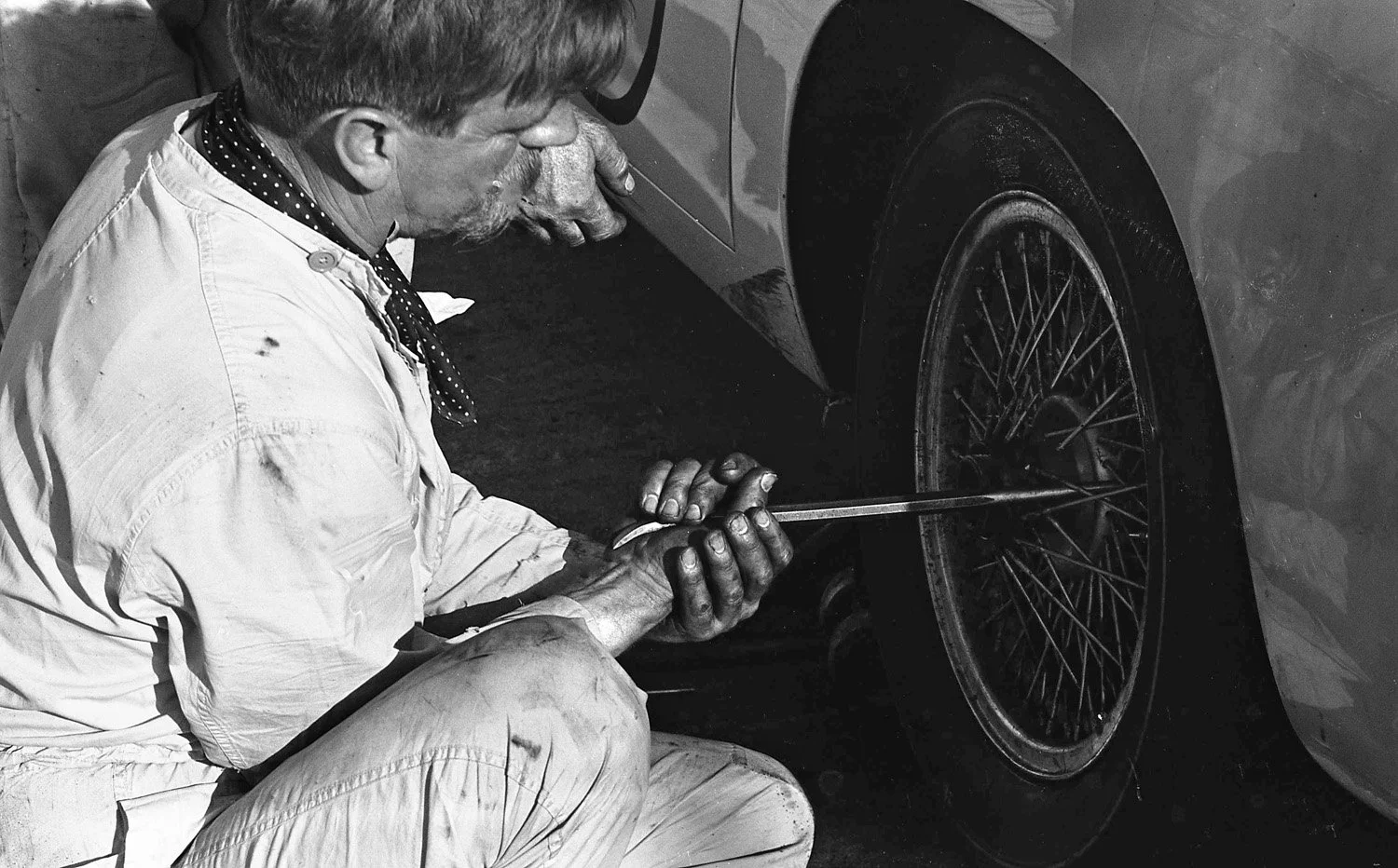  1961: Master Aston Martin mechanic Rex Woodgate is trying valiantly to loosen the wheel on one of the DB4 GTs.  The cars were sent with Borrani wire wheels to take wider tires but were so tight both cars went out with broken hubs due to overheating.
