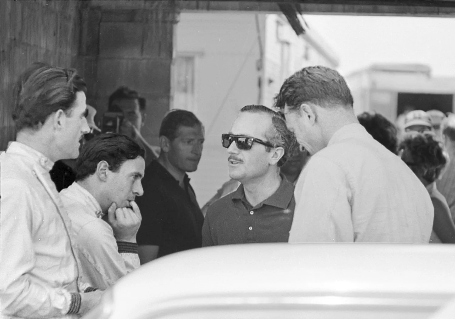  1964: Why are Graham Hill, Jim Clark, Colin Chapman and Dan Gurney in deep conversation?  Chapman is telling Hill he best get on the Indy program.  Clark and Gurney have already done it and Chapman thinks Hill can win it.  And he did 2 years later. 
