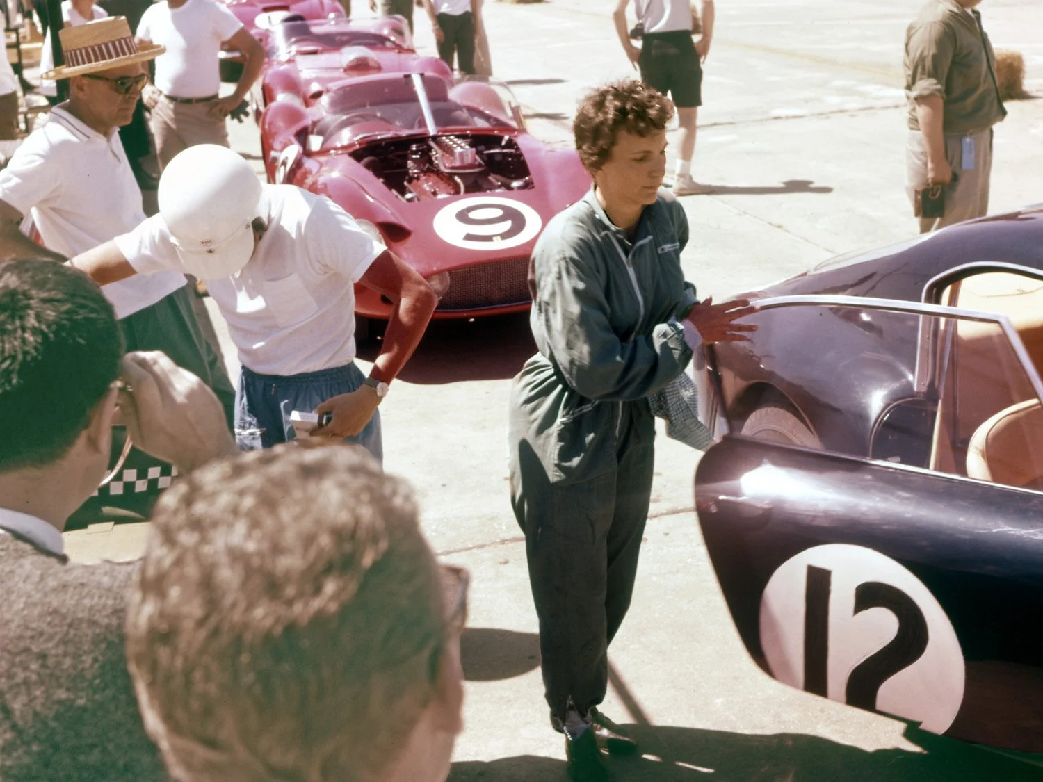  1961: Denise McCluggage is preparing her Ferrari Berlinetta.  Co-Driver Alan Eager, head down, is visualizing.  In a stunning race, the duo won the GT class over stout competition and drove the Ferrari back to New York on Monday. 
