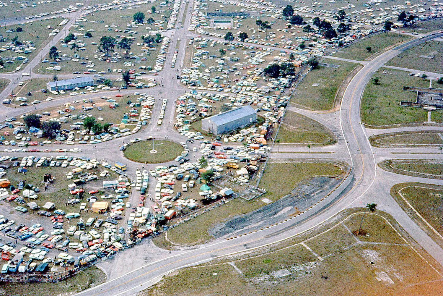  1964:  Sebring was growing faster than anyone expected.  An aerial view shows part of the 60,000 that attended.  The fences at the esses are wall-to-wall packed.  You can clearly see the outlines of the old barracks foundations. 