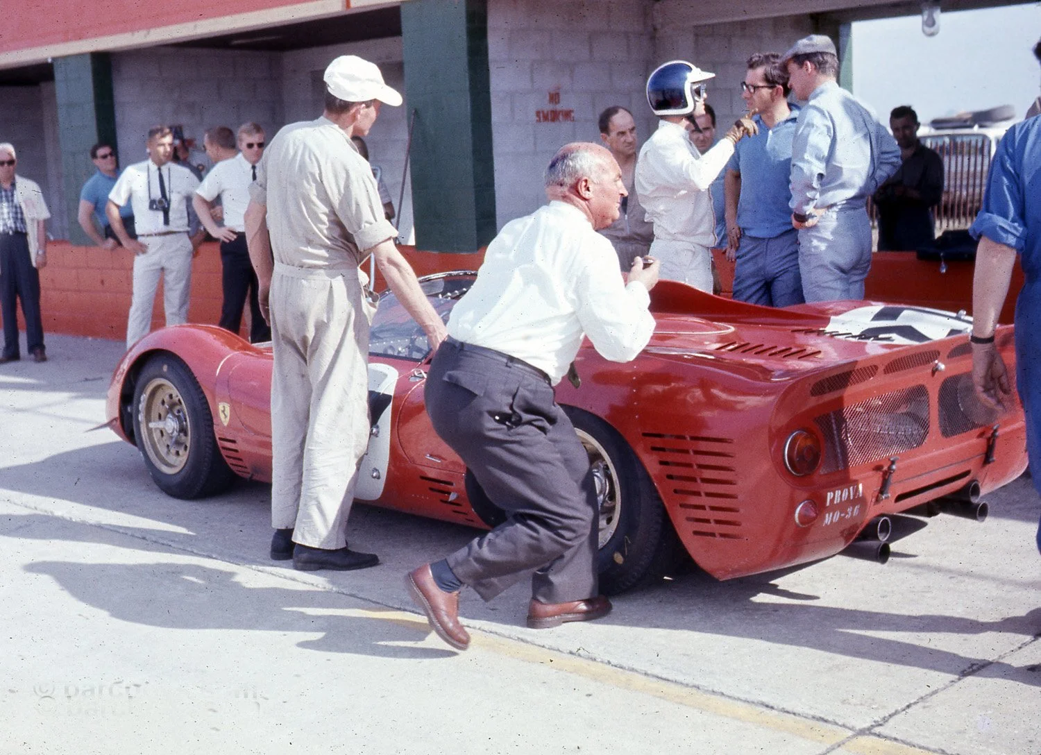  1966:  Bob Bondurant (as usual) is explaining the 330P to Mauro Forghieri and Mike Parkes.  Note Vic Barlow, competition manager at Dunlop checking his tires.  Ferrari switched from Englebert to Dunlop in the late 50’s and used their disc brakes. 