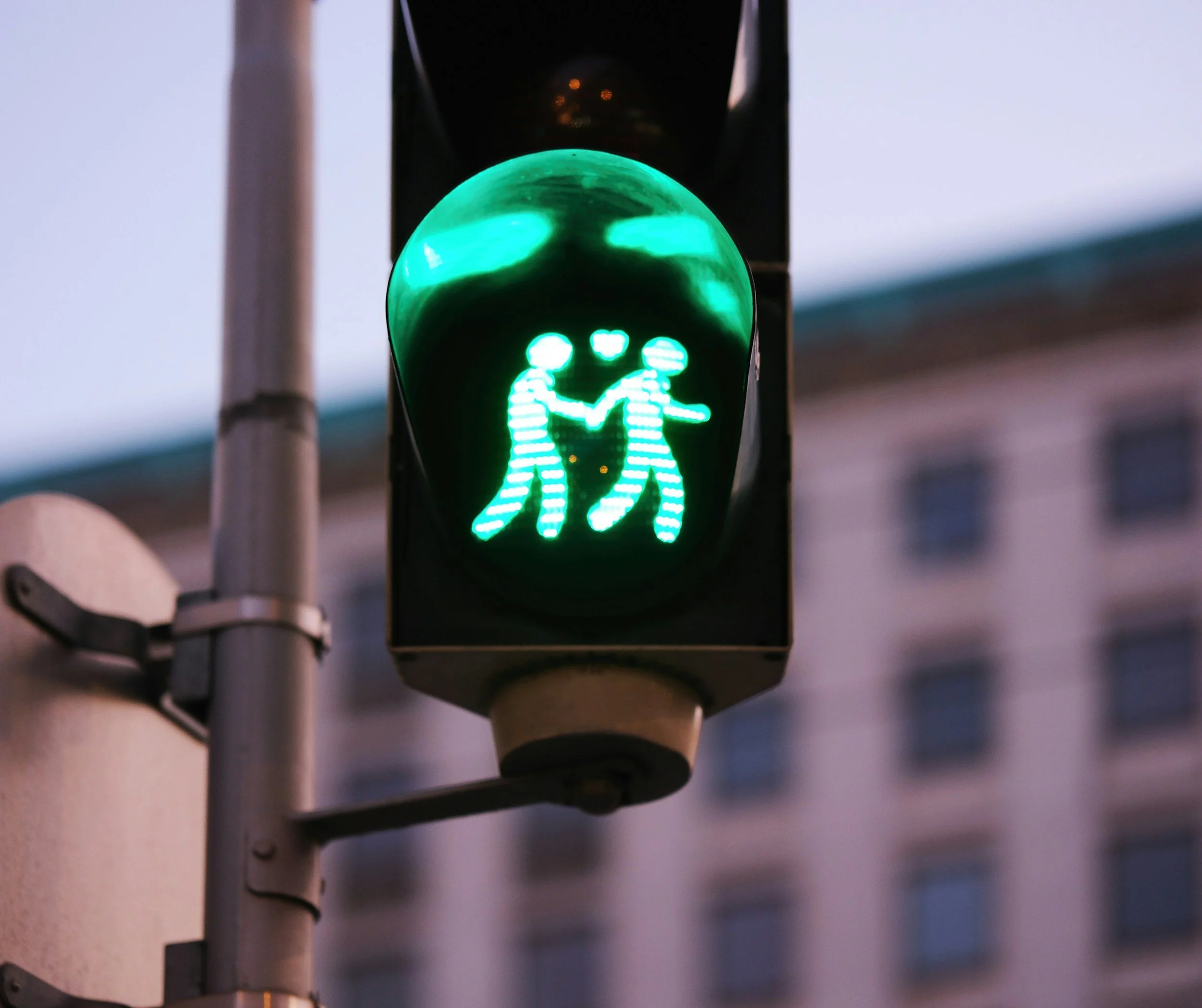 An innovative traffic signal designed like a stop sign, featuring a glowing green light that displays a graphic silhouette of a couple holding hands with a small heart floating between them.