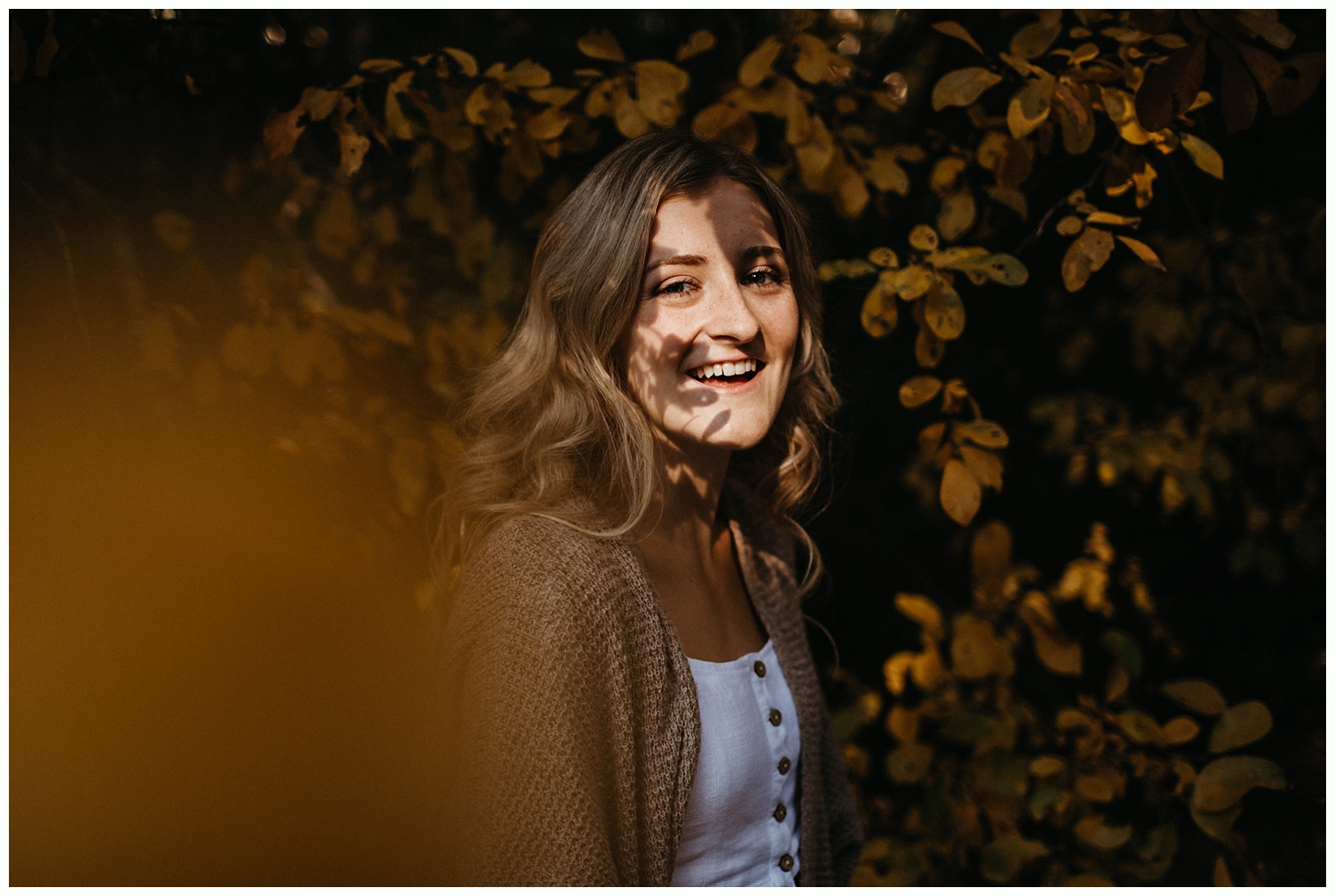  High school senior next to fall leaves smiling at camera. 