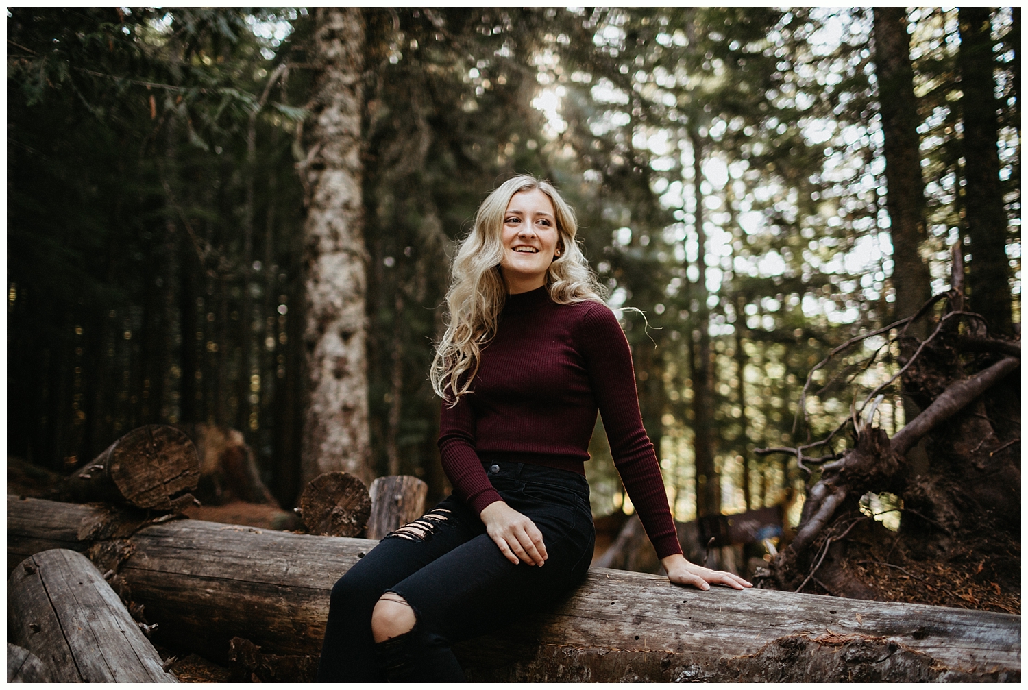  High school senior sitting on log in forest. 