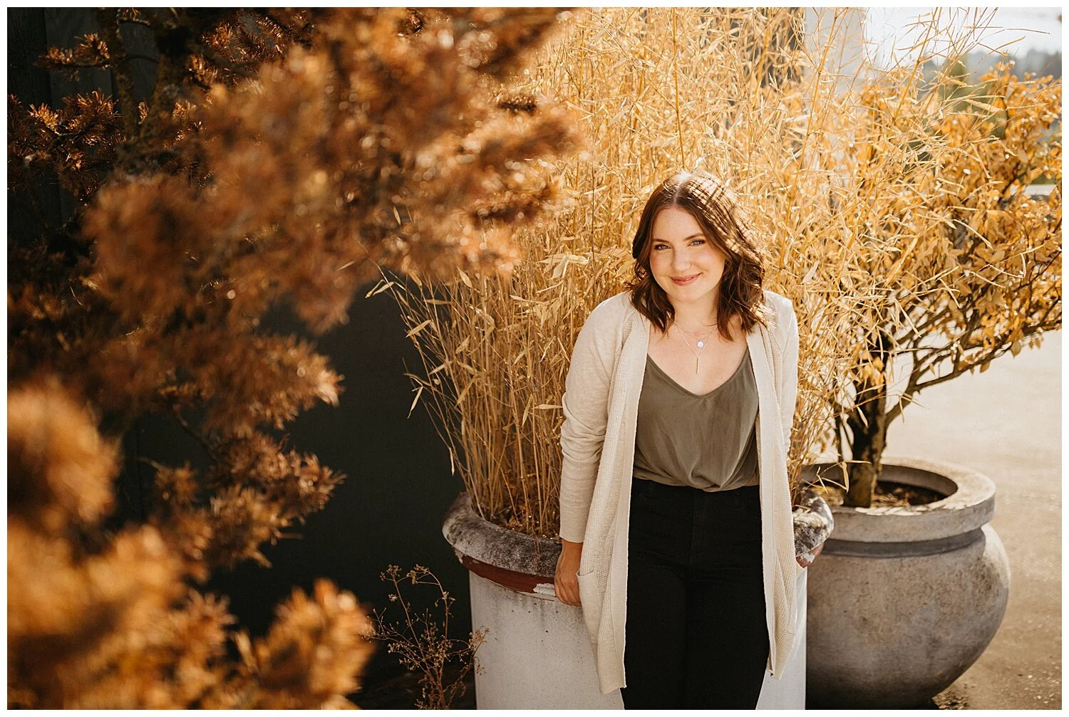 High school senior girl smiling in front of golden bush.