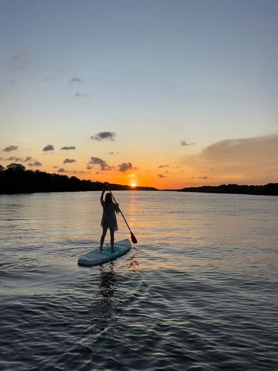 Person paddleboarding on a calm river at sunset.