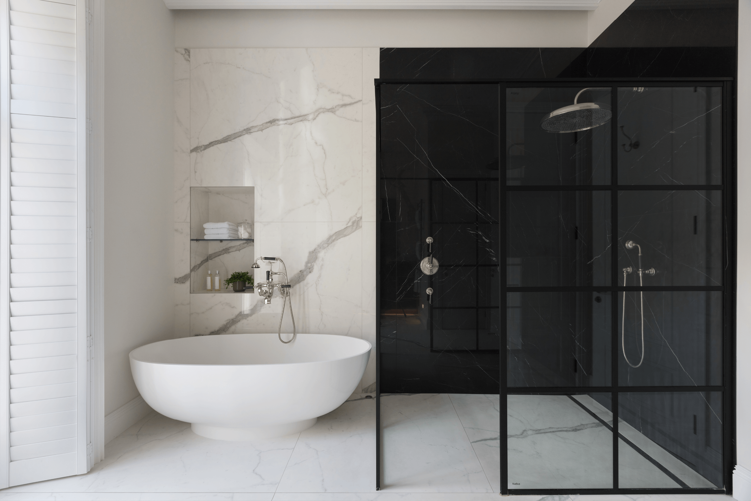 Luxury bathroom designed by Margot Tsim Interiors — freestanding white bath against Calacatta marble tiling with a black steel-framed shower enclosure and Nero Marquina marble, St John's Wood, London