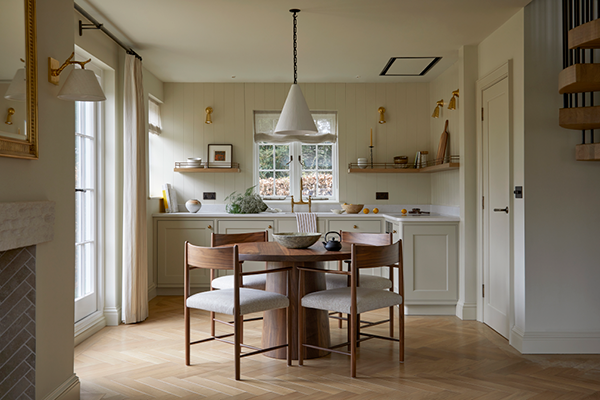 Kitchen with a round dining table, four chairs, white cabinets, and wall shelves holding decorative items, with natural light from windows.