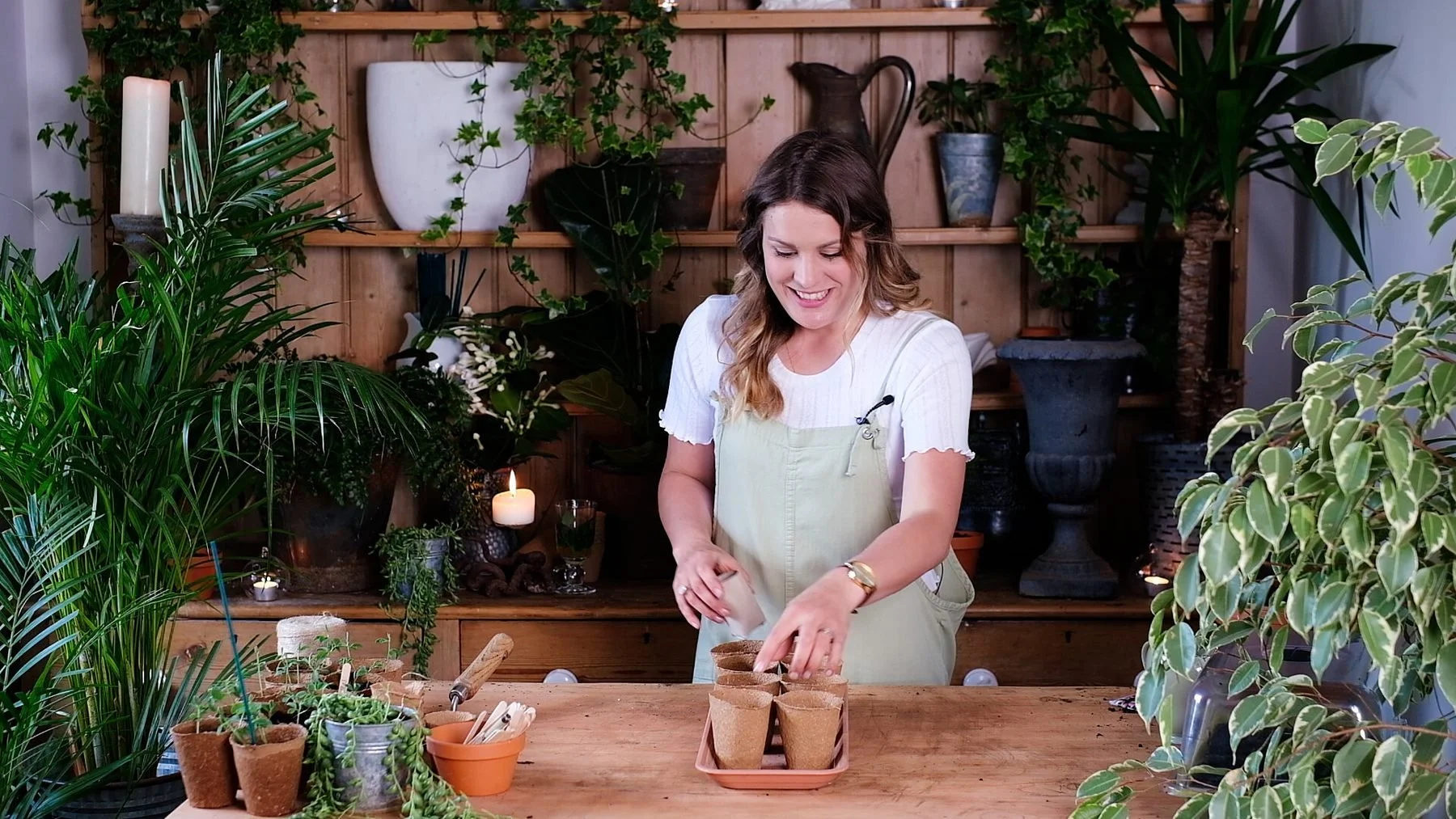 Alex at her potting table, filming a lesson surrounded by plants