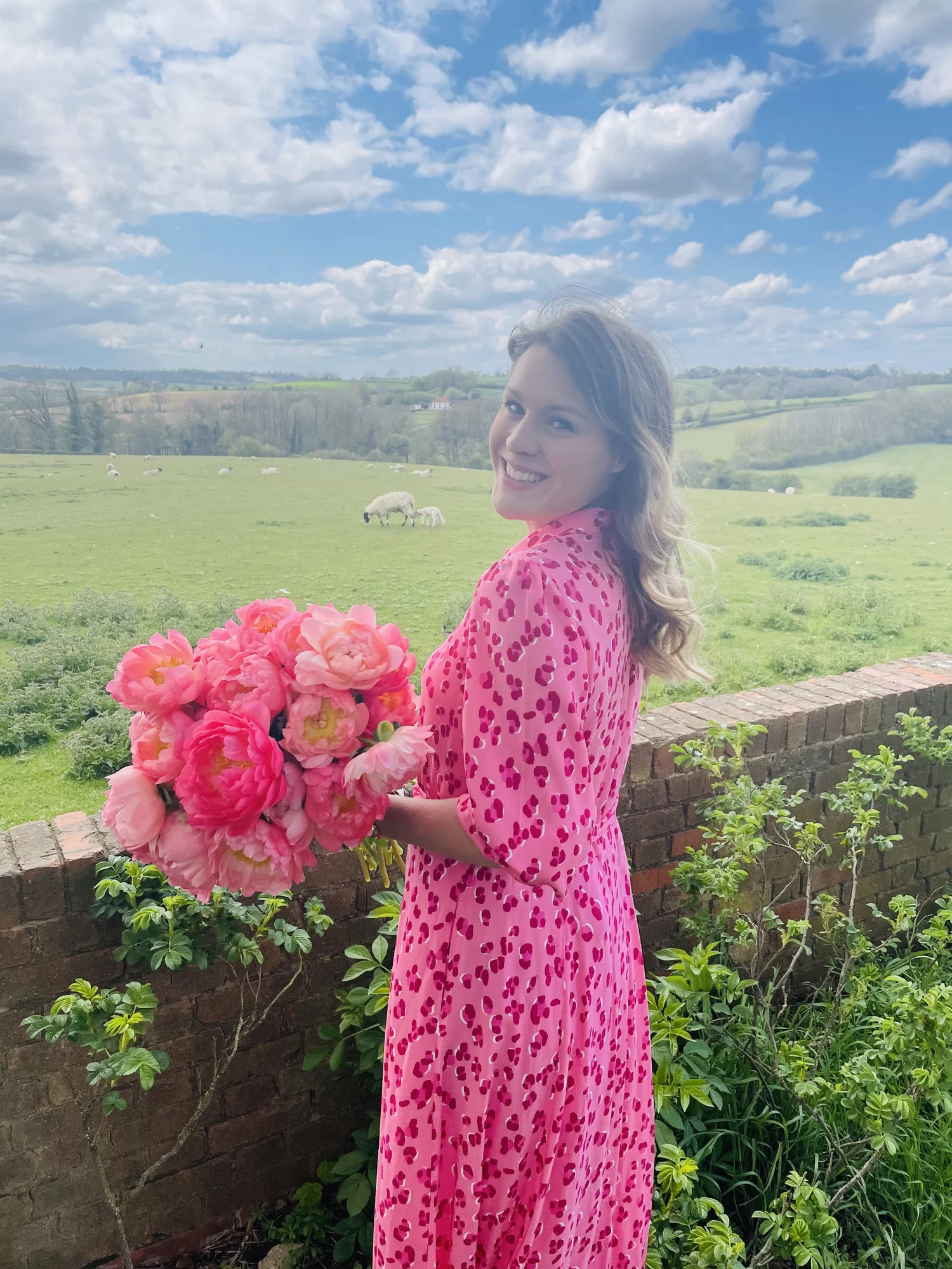 Alex in a pink dress holding a bunch of pink flowers in the countryside