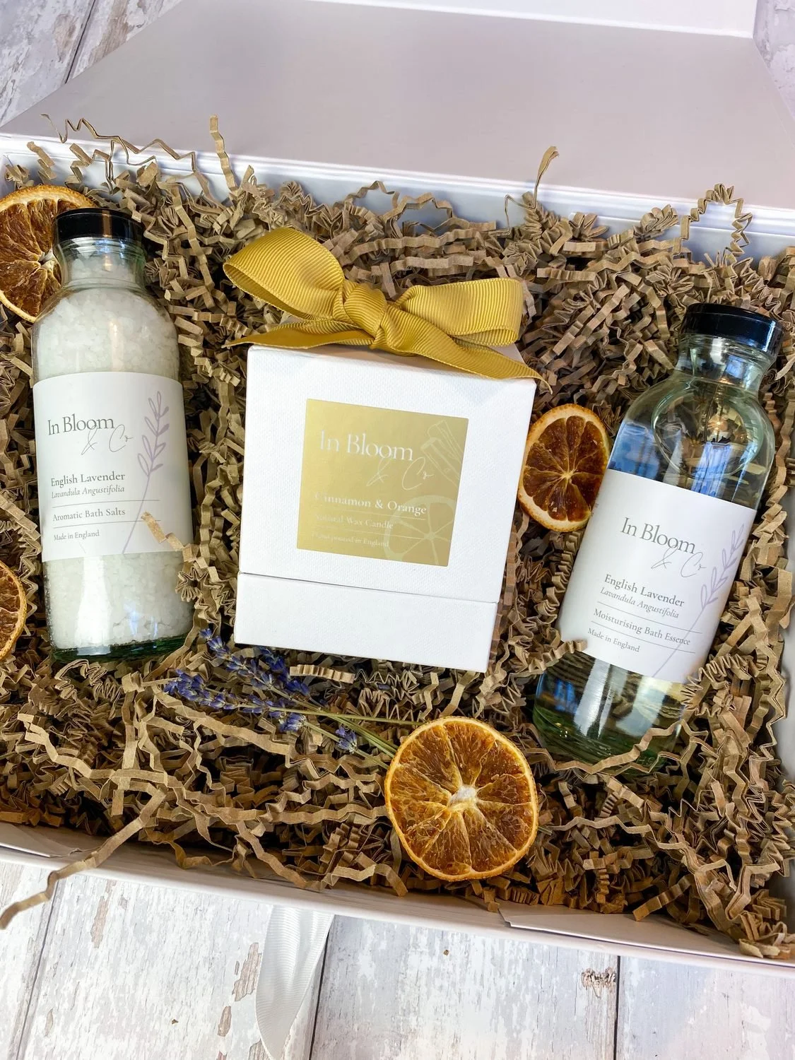 A gift box with botanical bath products and a candle, dried oranges and gold ribbon