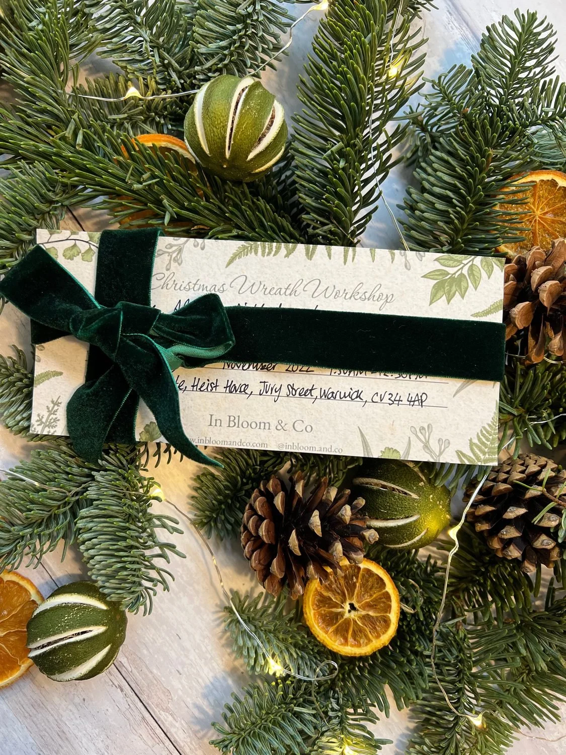 An In Bloom &amp; Co gift voucher with green velvet ribbon among dried oranges and pine cones