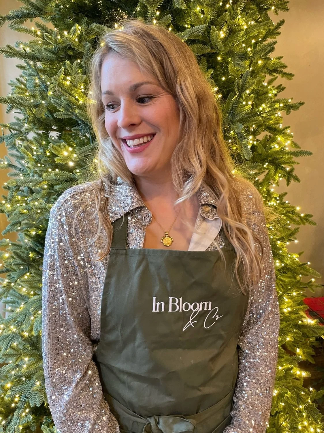 Alex in her In Bloom &amp; Co apron in front of a lit Christmas tree
