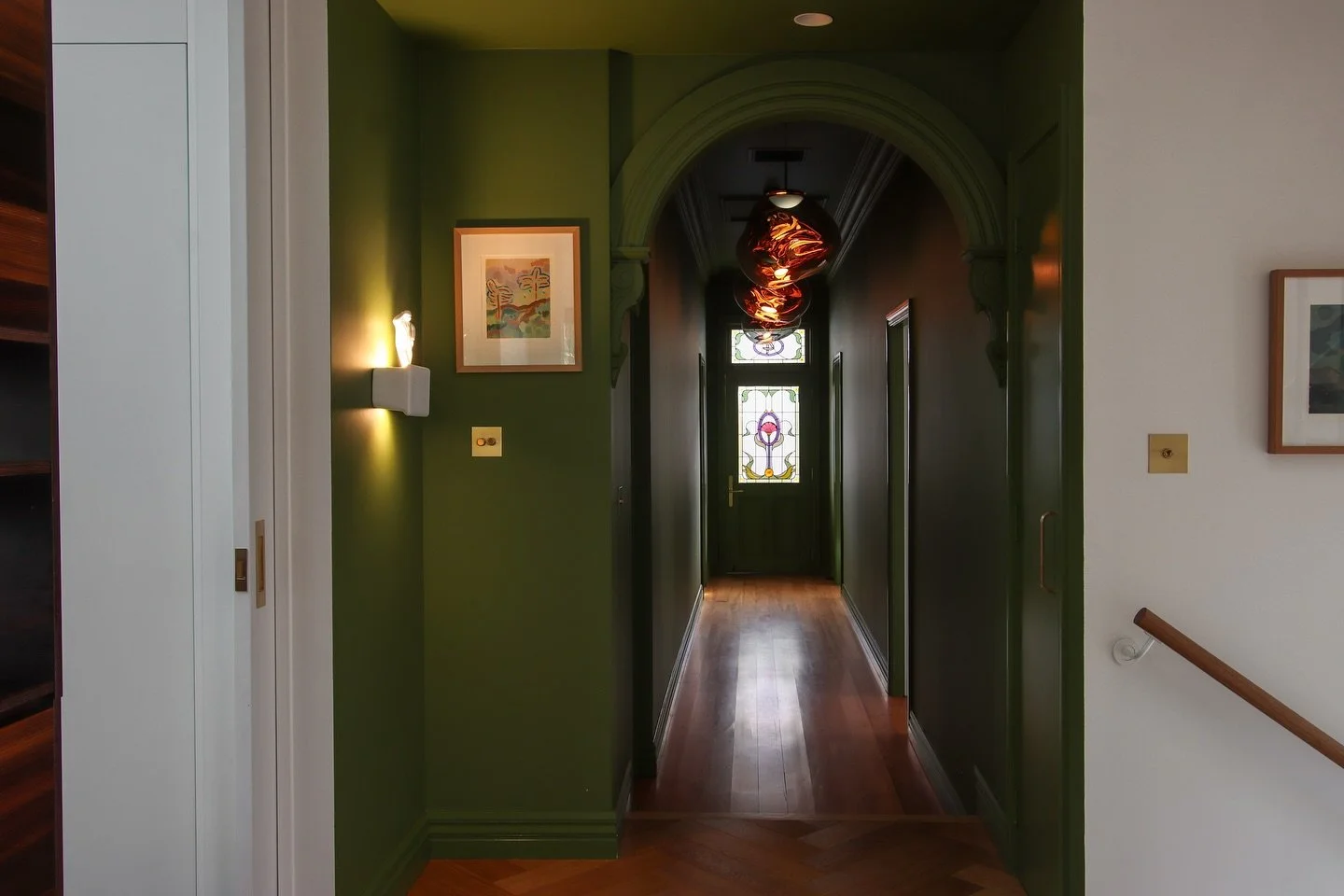 Open the yellow door and be greeted by a warm colour-drenched hallway, lit with handsome stained glass and striking pendants. 
Seamlessly coating the walls, trims, even ceilings and doors in a single colour creates an intentional, cohesive and visual