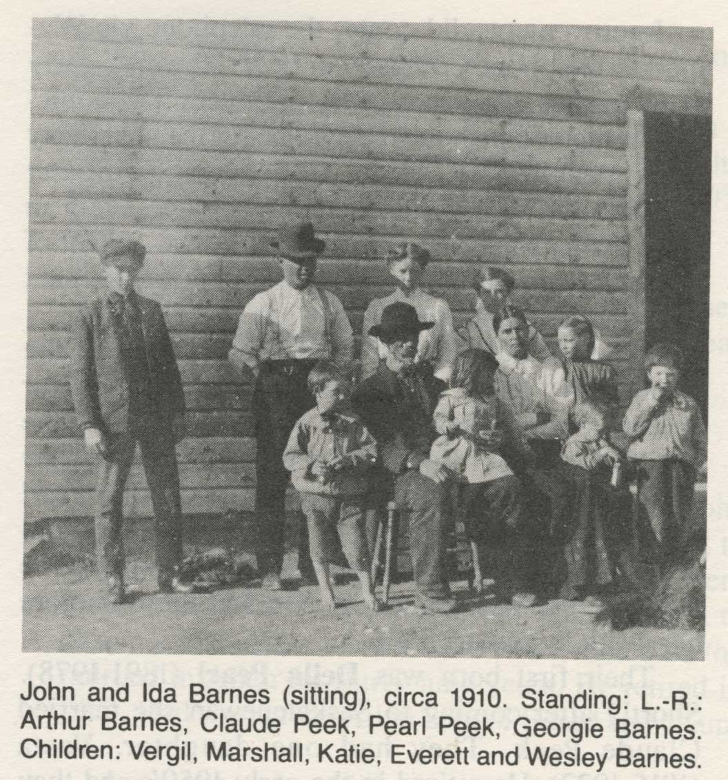  The Barnes family. Family poses outside farmhouse for photo. Older generations sitting, younger sitting on old people’s laps. Older children standing behind their elders.  