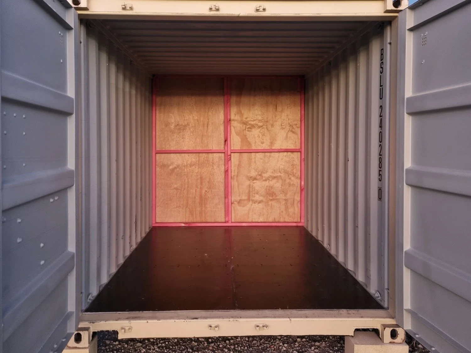 Empty shipping container with wooden paneling at the back and black flooring inside.