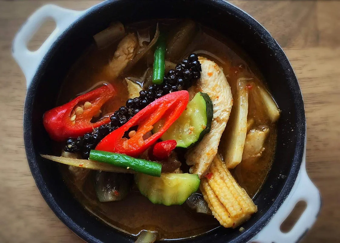 Vegetable curry in a black pot with baby corn, red chili peppers, cucumbers, and green beans