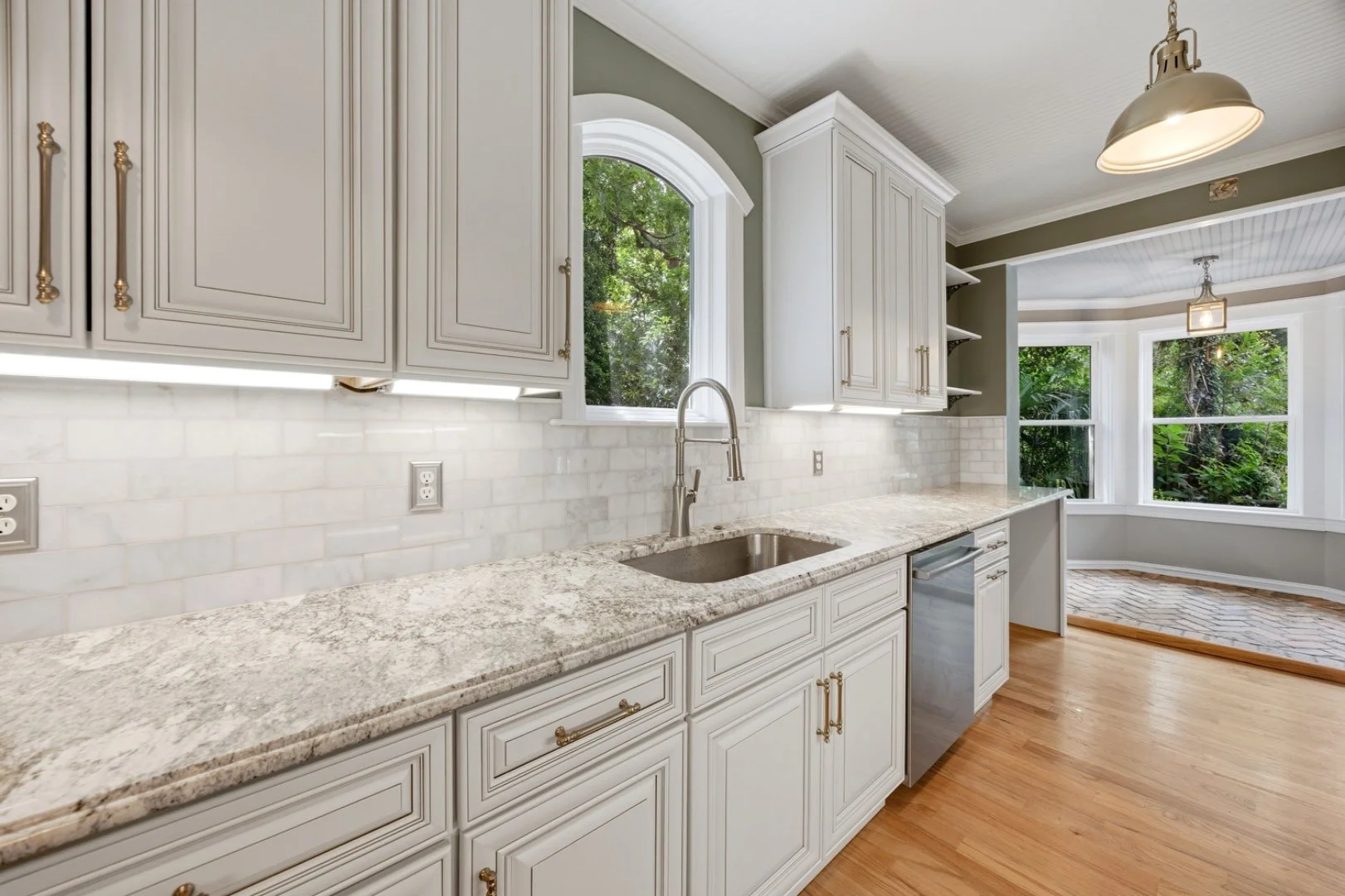 Custom cabinetry with granite countertops and a marble subway tile backsplash, framed by an arched window.