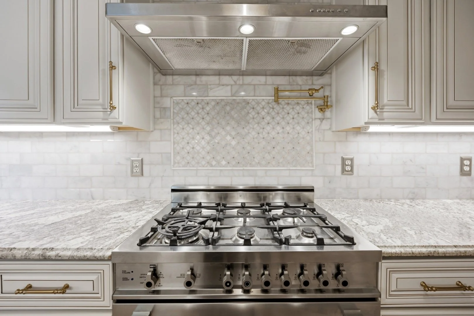 A custom range hood surround with marble mosaic tile and a brass pot filler.
