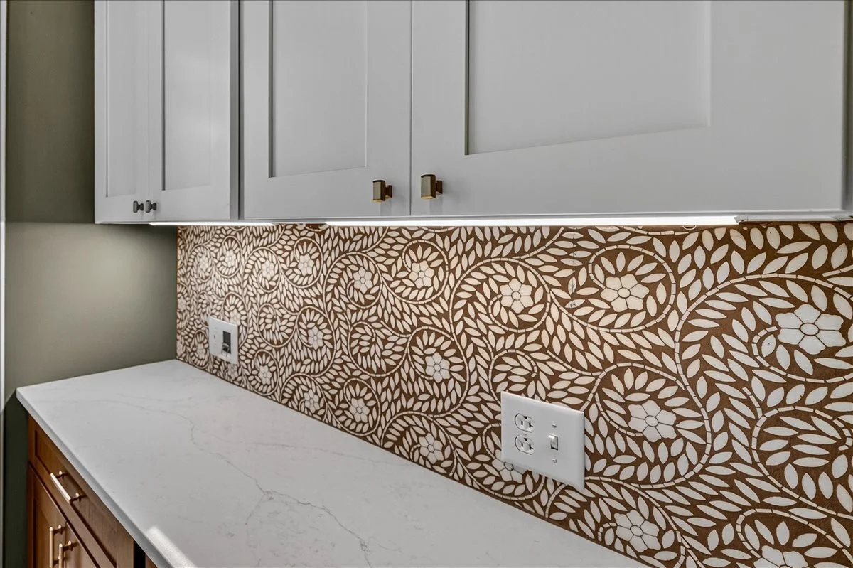 Detail of a custom mosaic tile backsplash beneath white shaker cabinetry.