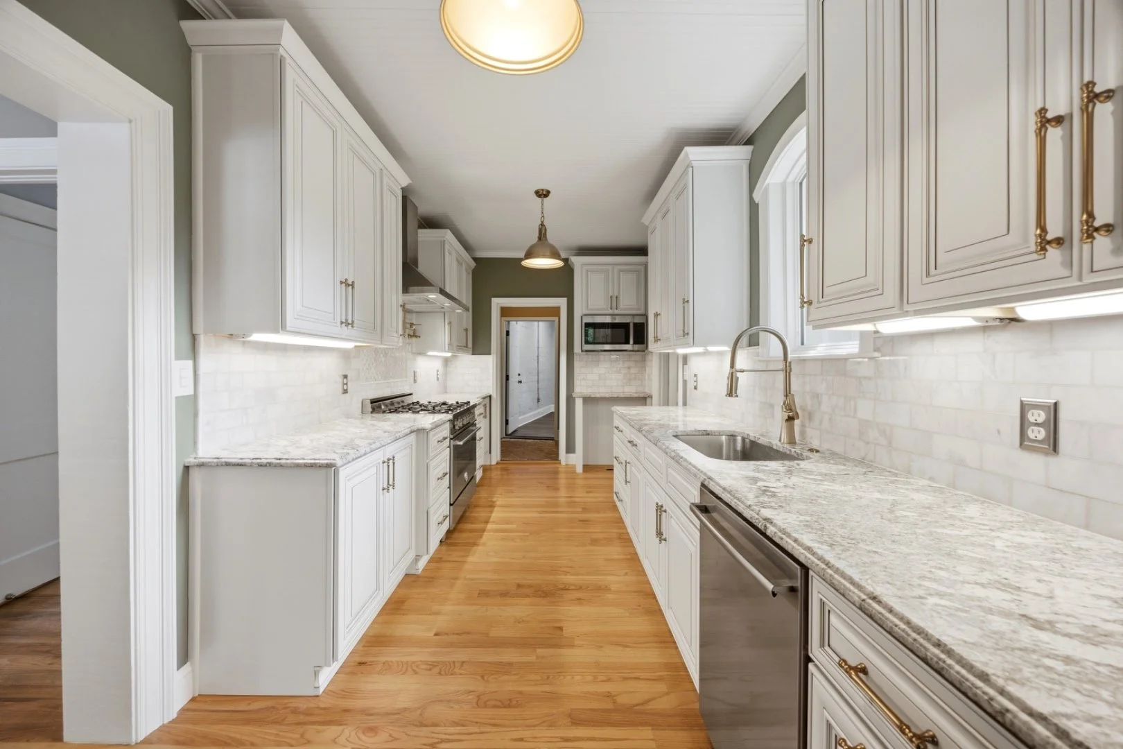 A bright galley-style kitchen finished with custom cabinetry, granite counters, and hardwood floors.