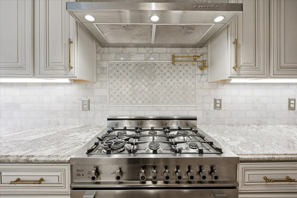 White MCW cabinetry framing a stainless steel range and decorative tile inset