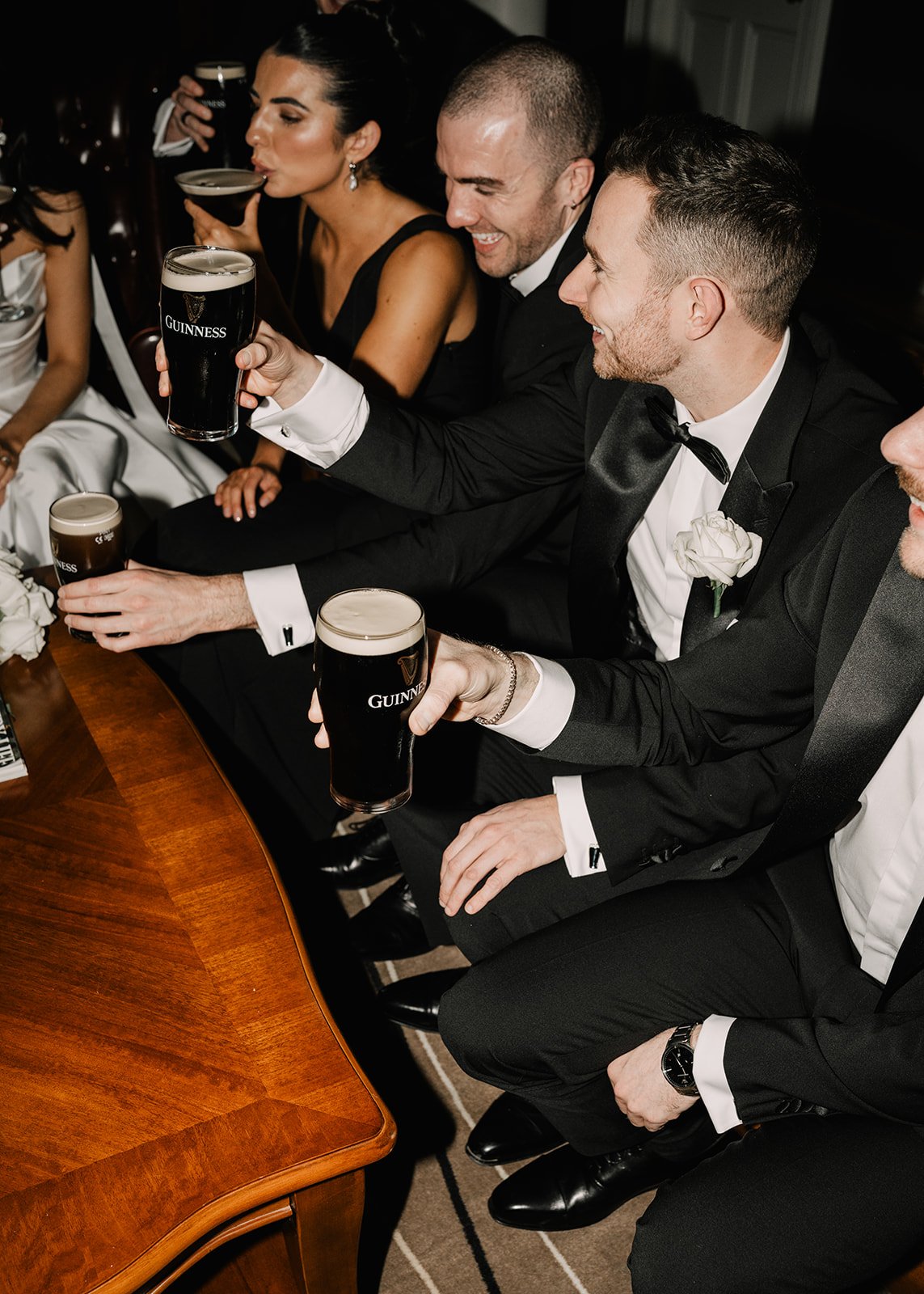 People dressed in formal attire sitting at a table, holding pints of Guinness beer, celebrating at a social event.