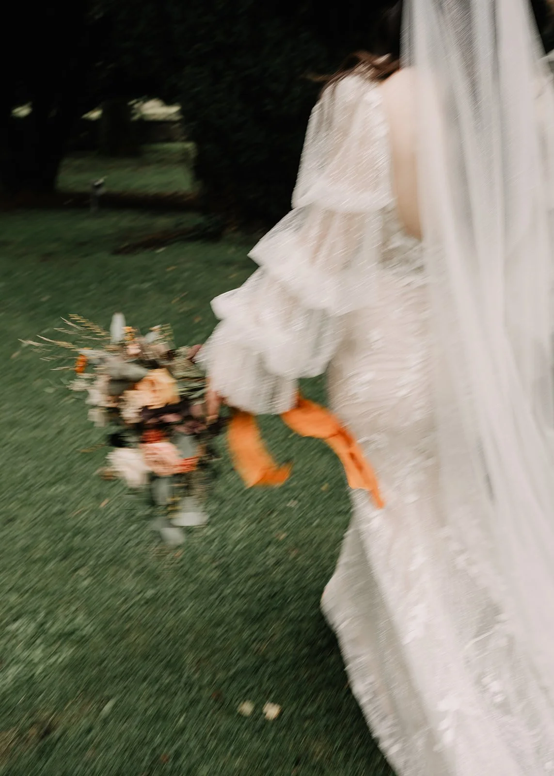 A person in a white dress holding a bouquet of flowers outside on grass, with trees in the background.