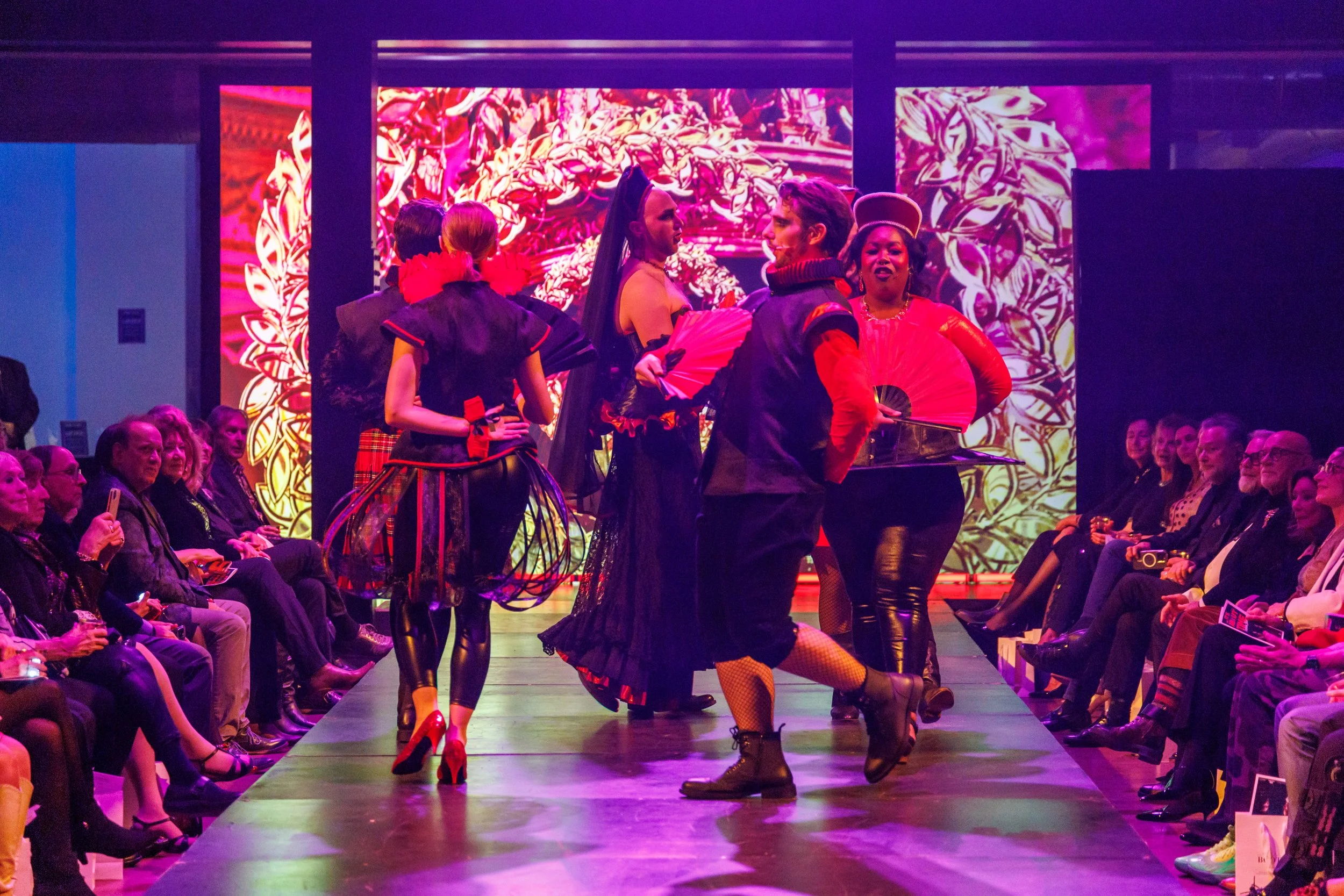 People dressed in colorful costumes walking on a runway in front of an audience at a fashion show.