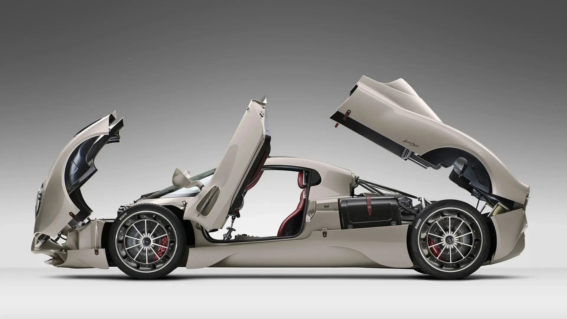 A silver sports car with its doors, hood, and trunk open, revealing interior and engine components, against a gray background.